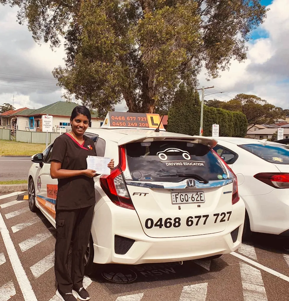 Female student holding license certificate next to Road Master car