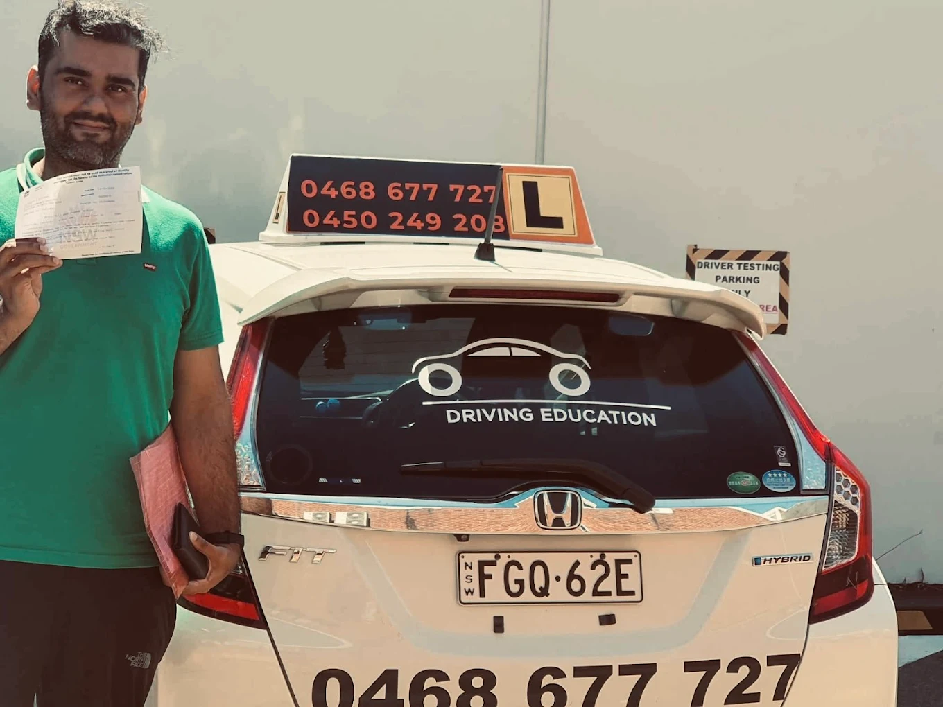 Male student in green shirt with certificate at back of car