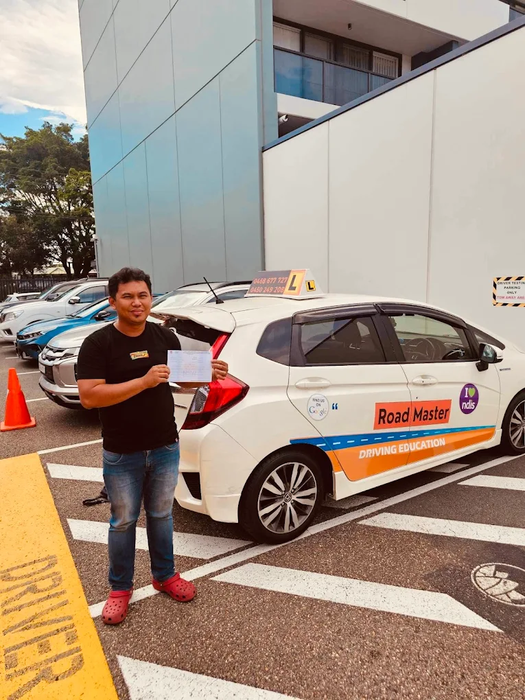 Male student in dark clothing with certificate in parking area